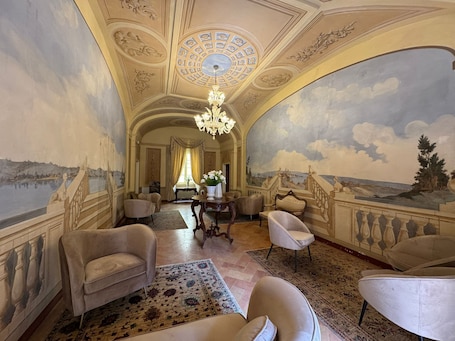 A luxurious room with a grand chandelier, elegant furniture, and a scenic mural on the walls.