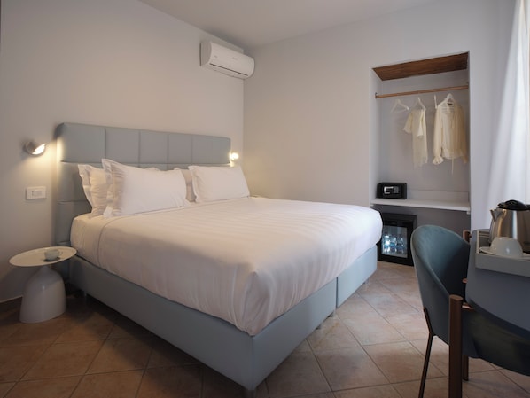 Una habitación de hotel con cama, mesita de noche, silla y un escritorio pequeño con hervidor.