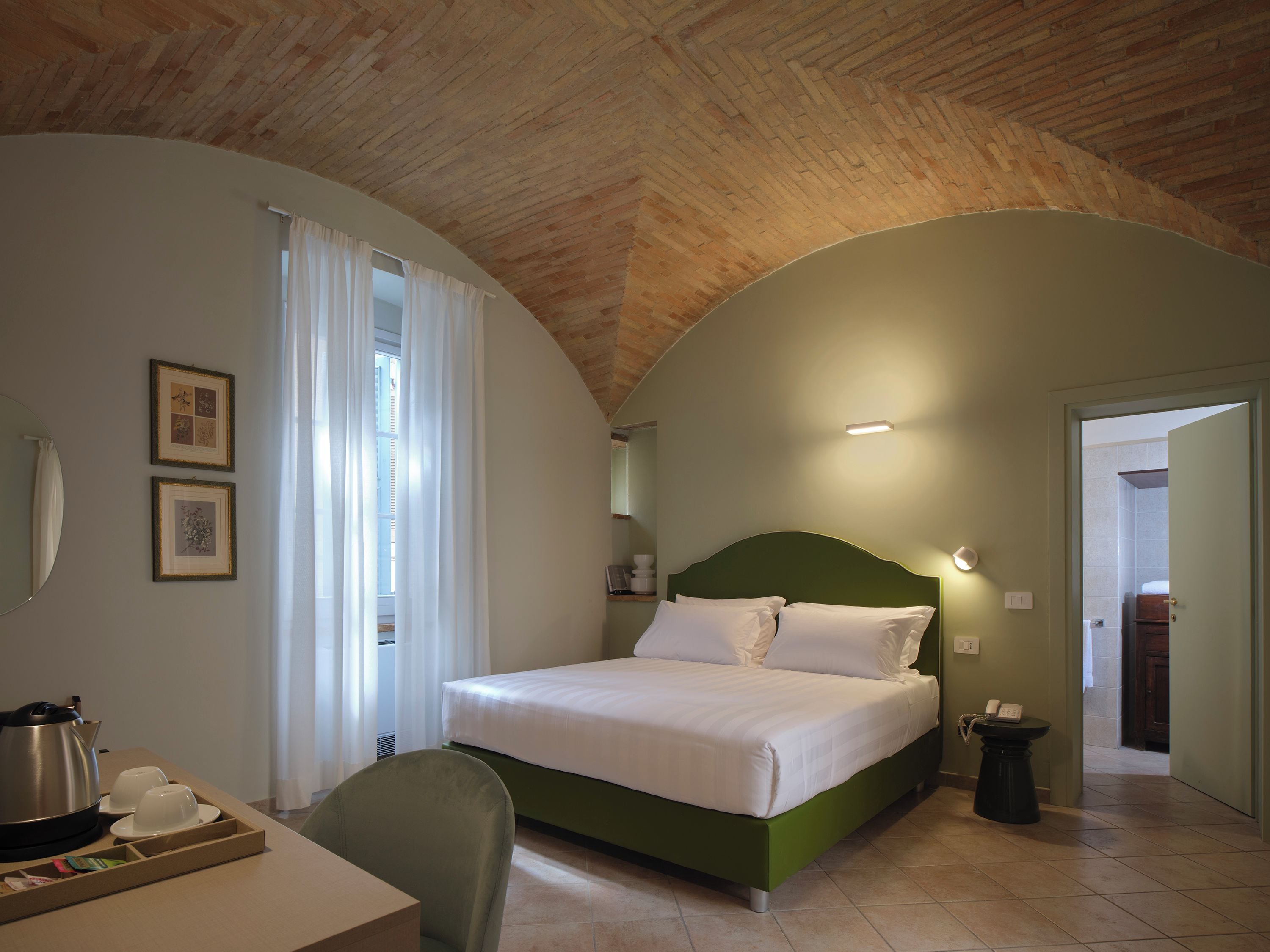A bedroom with a bed, a desk with a kettle, and a chair.