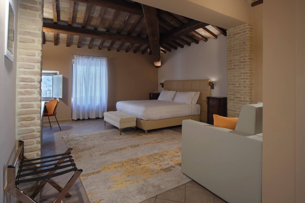 Un dormitorio con cama, sofá, sillón, escritorio y ventana con cortinas.