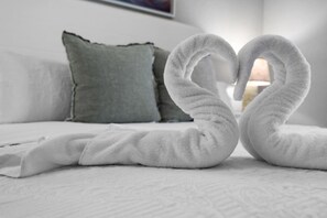 Een bed met witte lakens en twee handdoeken gevouwen in de vorm van een hart.
