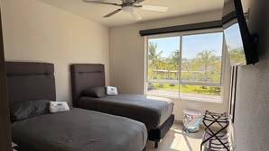 A bedroom with two beds, a ceiling fan, a large window with a view, and a TV mounted on the wall. - Fabulous Apartment at Dream Diamante Acapulco (Acapulco)