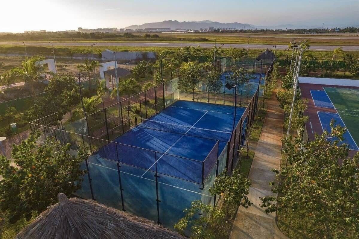 Een tennisbaan omringd door groen, met uitzicht op een verderop gelegen vliegveld en landschap.