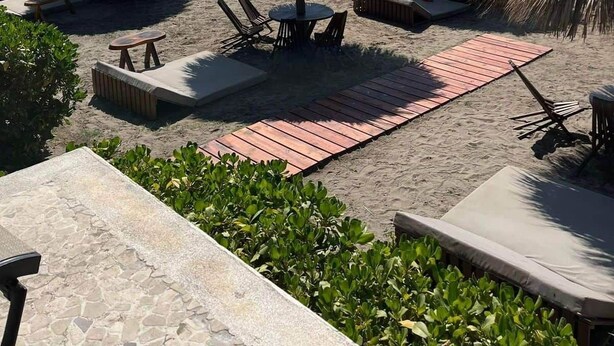 Un espace de détente aménagé sur la plage, avec des parasols en chaume, des chaises longues et une terrasse en bois.