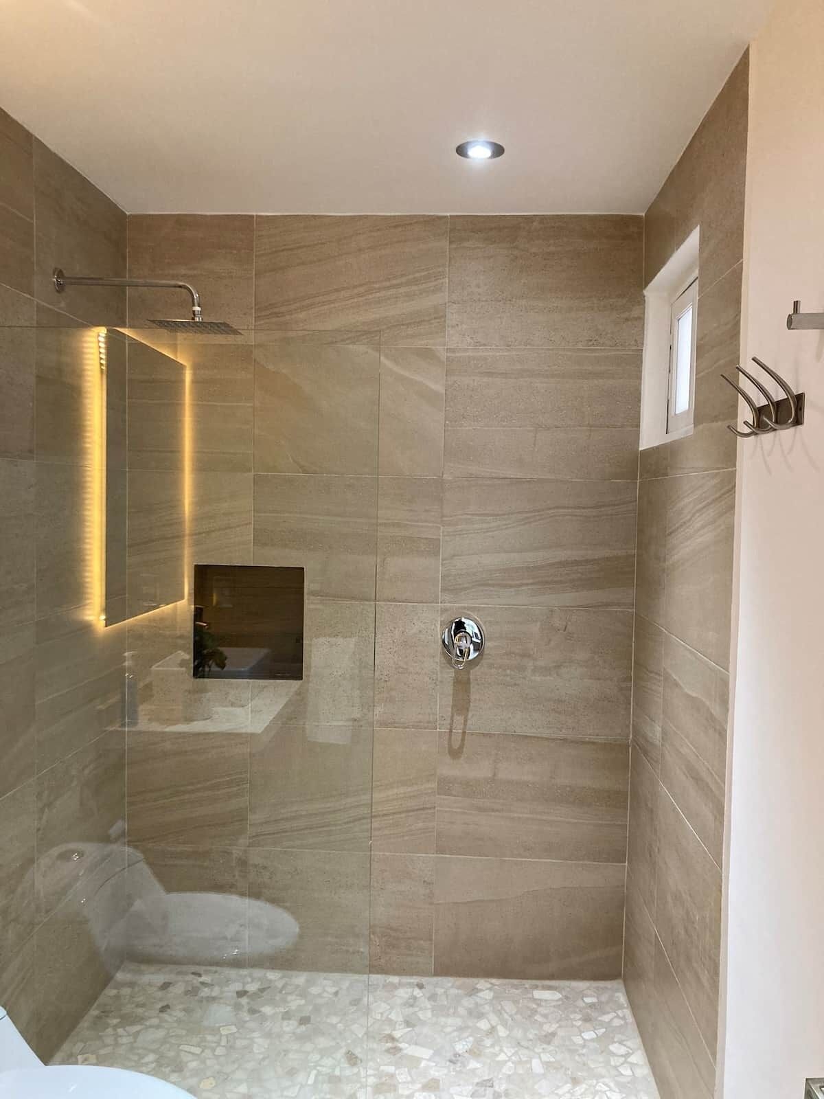 A modern bathroom with a glass-enclosed shower, a built-in sink, and a small window.