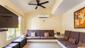 A living room with a sofa, a television, an air conditioner, and a ceiling fan.