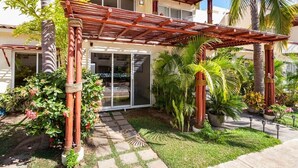 A two-story building with a covered patio, palm trees, and potted plants.