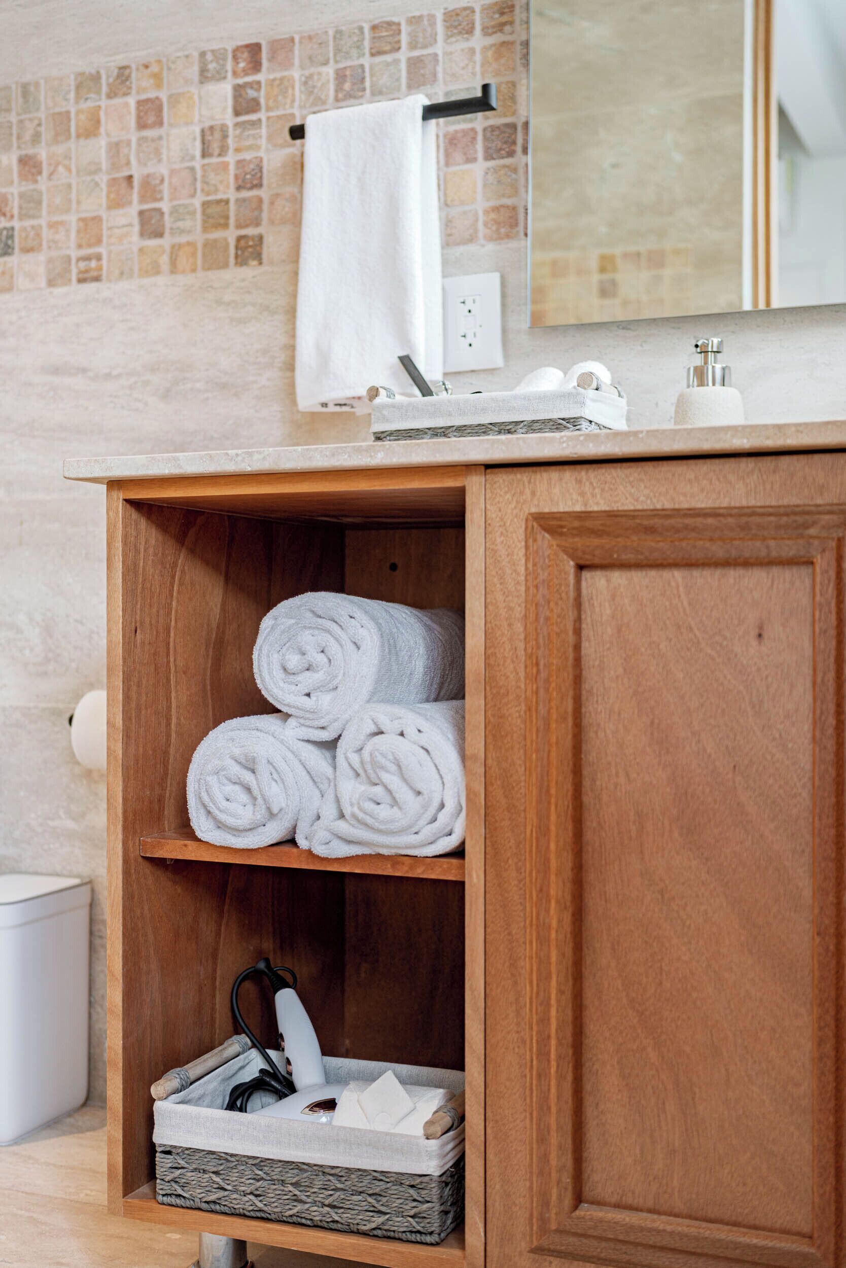 A wooden vanity with a mirror, a towel rack, and a shelf with rolled towels and a basket.