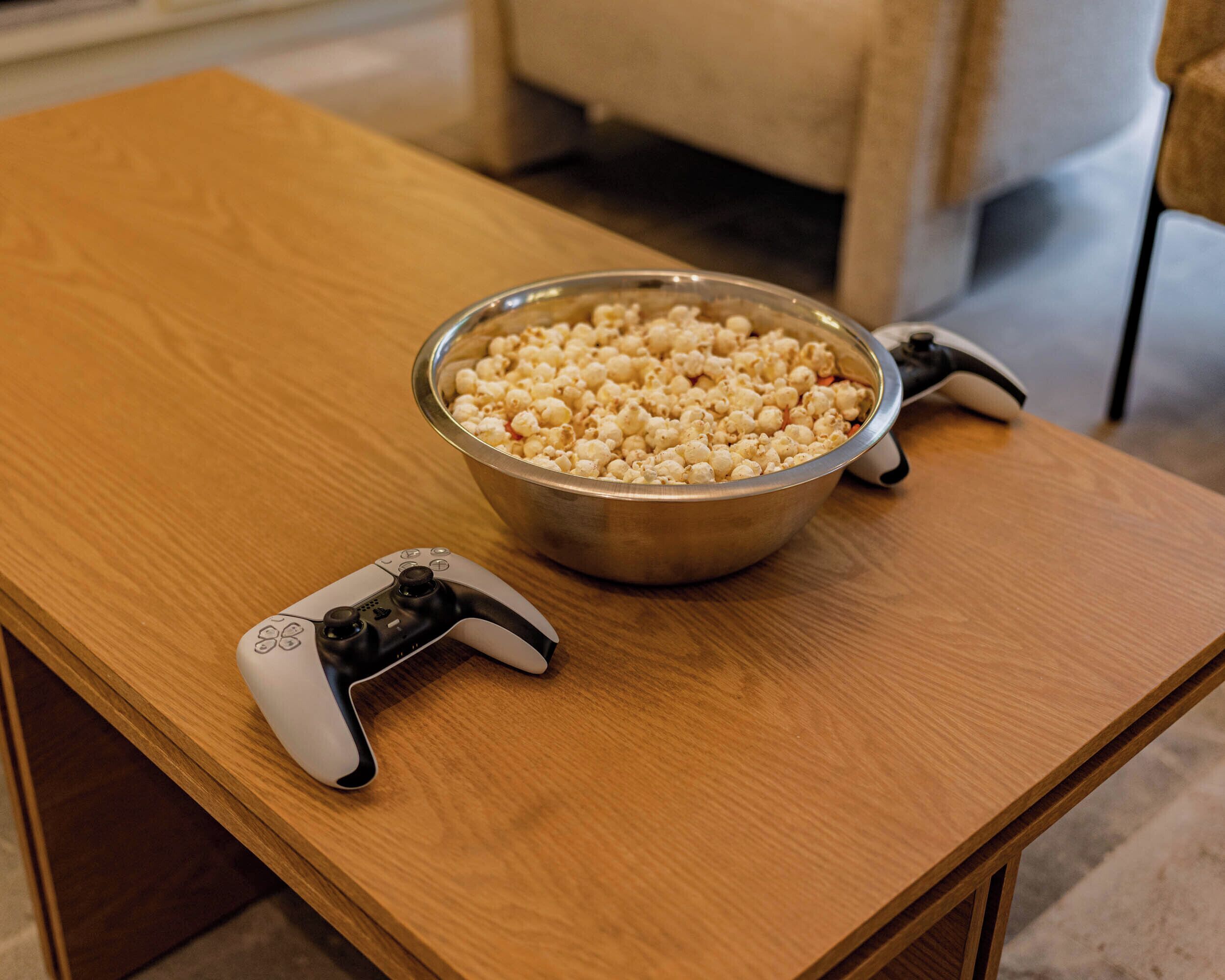 Un tazón de palomitas de maíz y un control de videojuegos sobre una mesa de madera.
