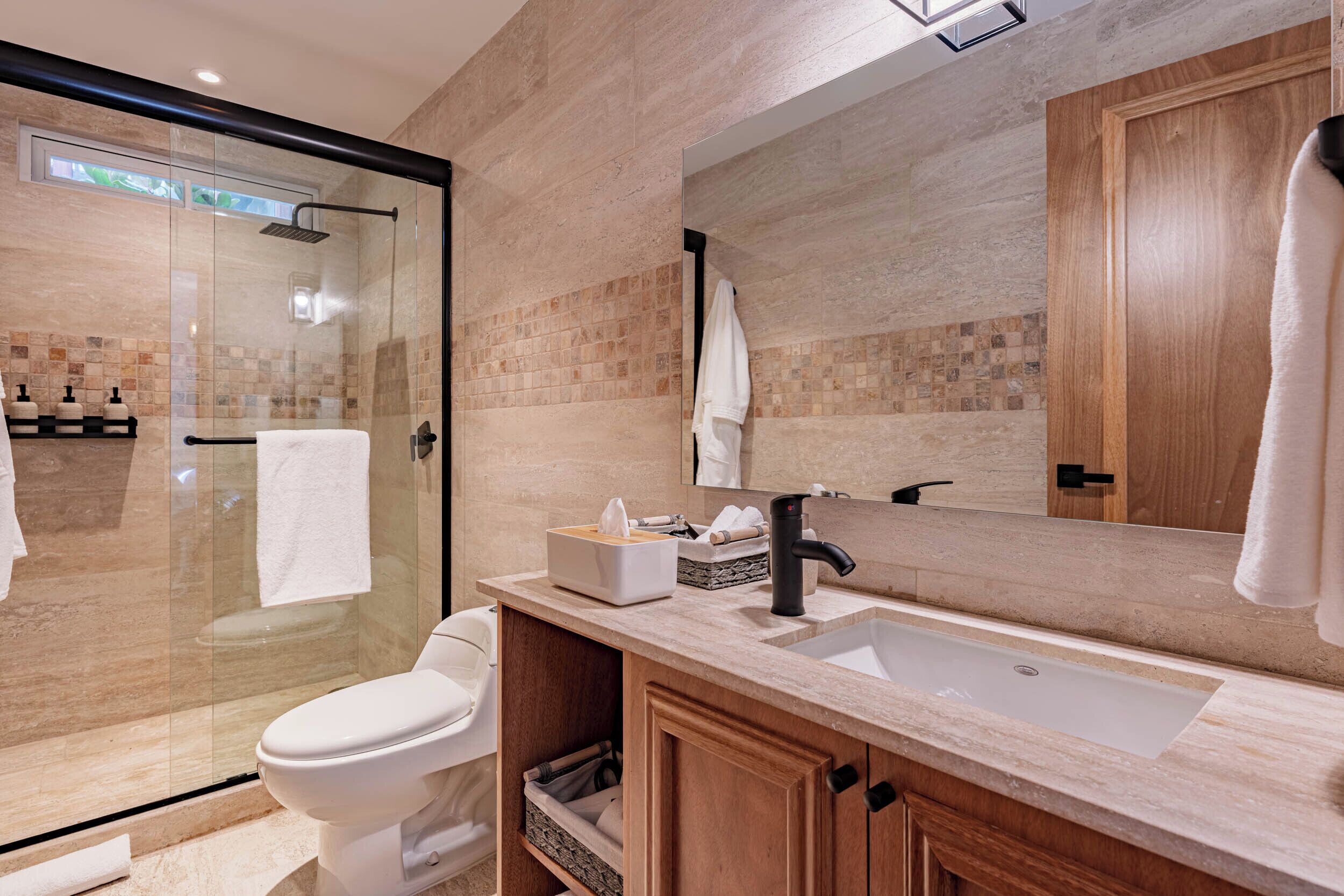 A modern bathroom with a glass-enclosed shower, a white toilet, a wooden vanity with a sink, and a large mirror.