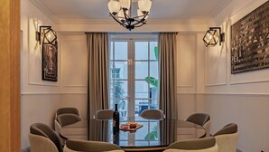 Een eethoek met een ronde tafel, zes stoelen, een kroonluchter en een raam met gordijnen.