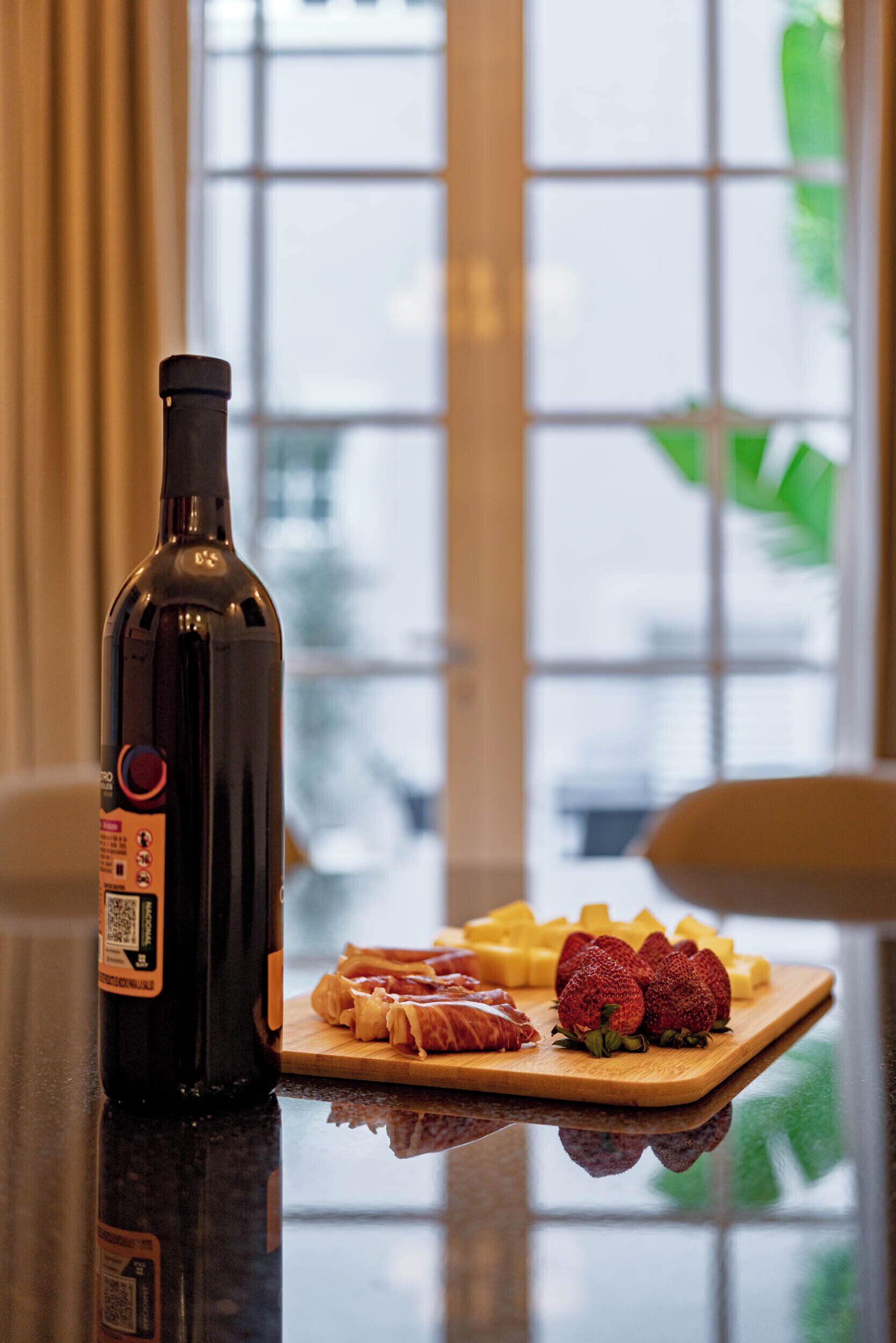 A bottle of wine on a table with a cheese board and strawberries.