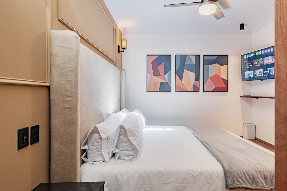 Ein Hotelzimmer mit einem Bett, einem Deckenventilator, einem Fernseher und abstrakter Wandkunst.