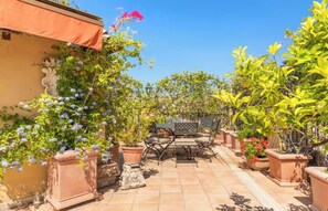 Une terrasse avec une table et des chaises, entourée de plantes en pot et bordée d’un mur jaune.