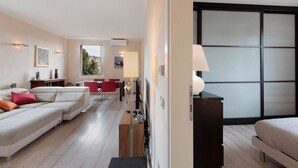 A modern living room with a sectional sofa, a dining area with red chairs, and a large window.