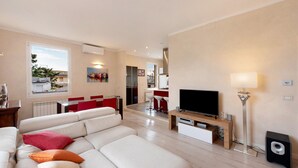 A modern living room with a sofa, TV, and a dining area in the background.