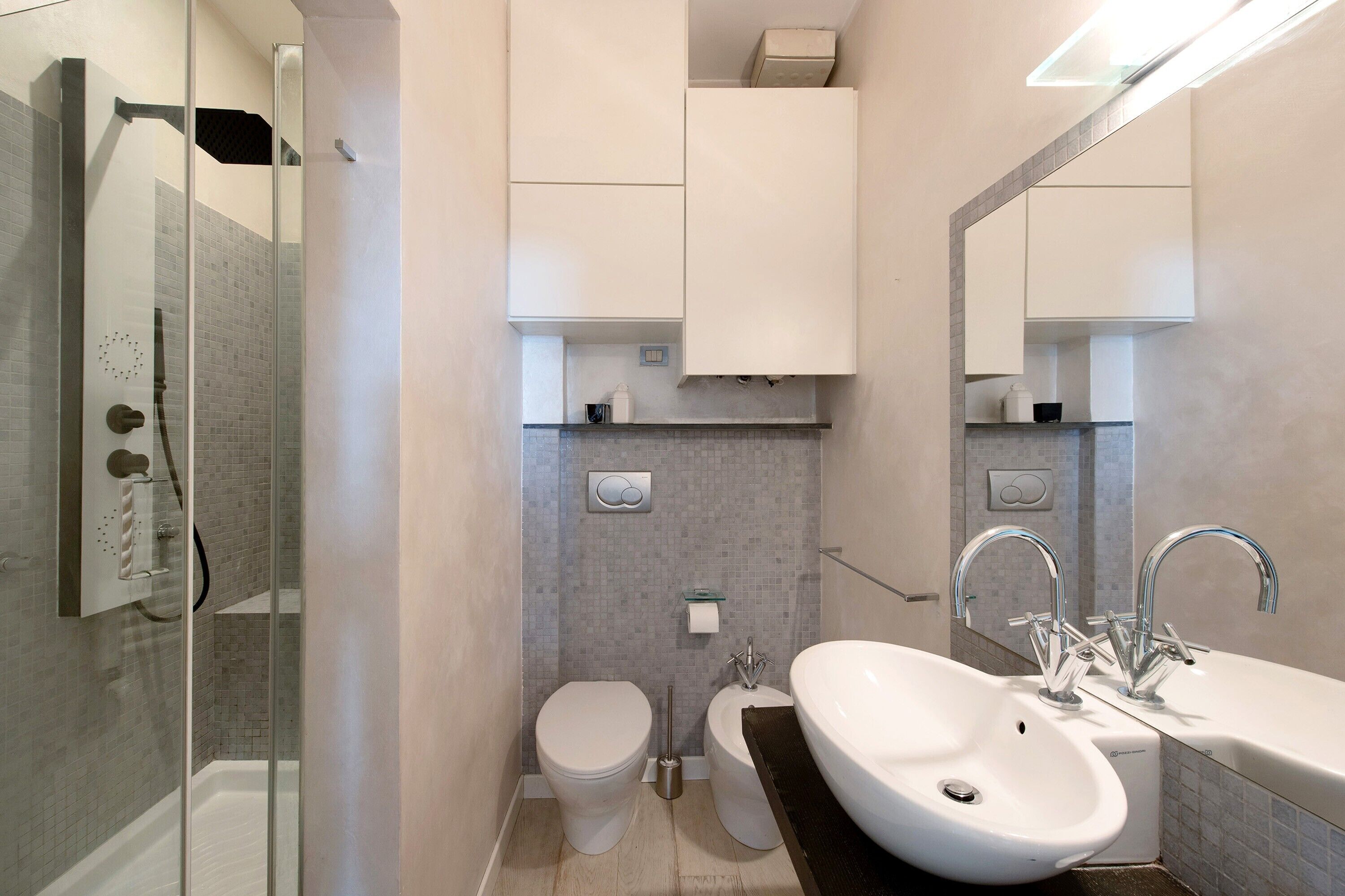 Ein modernes Badezimmer mit Duschkabine aus Glas, einem weißen Waschbecken mit großem Spiegel und einer Toilette.