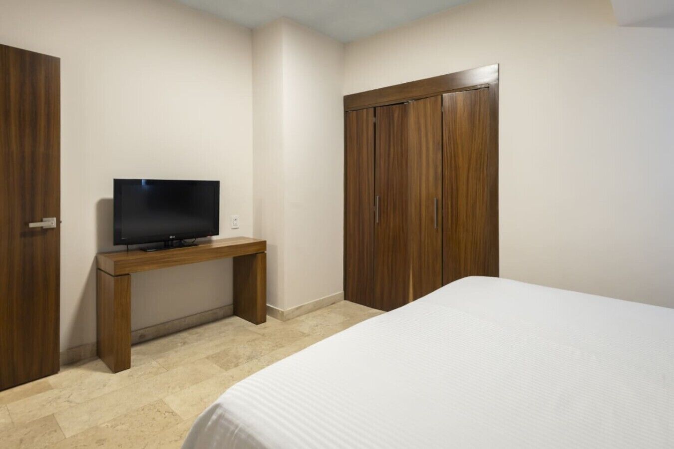 A hotel room with a bed, a TV on a wooden stand, and a wardrobe.