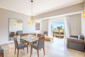 A spacious living room with a glass dining table, grey sofas, and a balcony with a view.