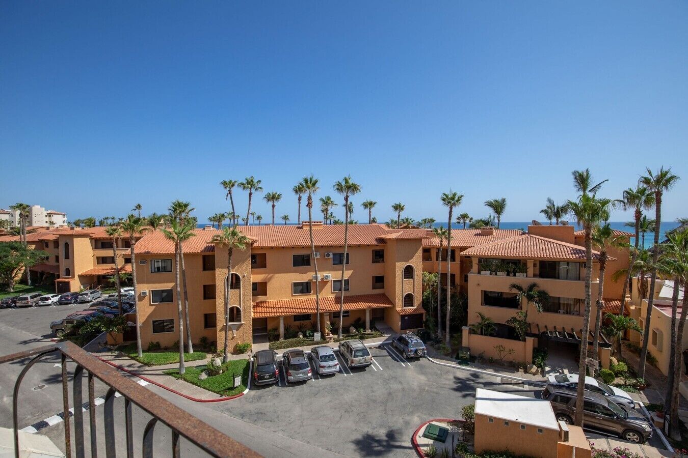 A multi-story hotel with a parking lot, palm trees, and a clear view of the ocean.