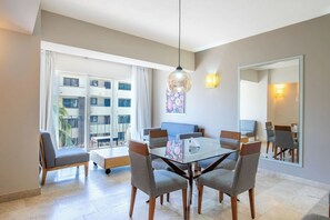 A modern dining area with a glass table, grey upholstered chairs, a large mirror, and a view of a building through large windows. - Depto a 5 min del mar y el centro de San Jose 102 (San José del Cabo)