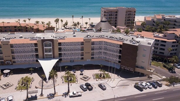 Un hotel con un patio central, varios pisos y vista a la playa y al océano.