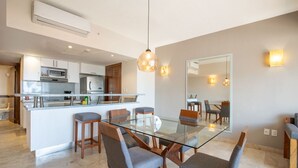 Une cuisine moderne équipée d’appareils électroménagers en acier inoxydable, une table à manger en verre avec des chaises, et un grand miroir.