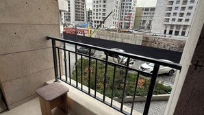 Varanda com duas bancos de madeira e guarda-corpo de metal, com vista para um canteiro de obras com edifícios altos e uma grua.