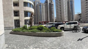 Uma área urbana moderna com edifícios altos, um calçadão pavimentado e veículos estacionados.