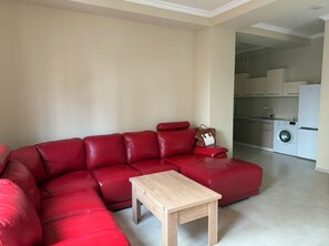 A living room with a red sectional sofa, a wooden coffee table, and a kitchen area visible in the background. - Your appartment in the center of Yerevan! (Yerevan)