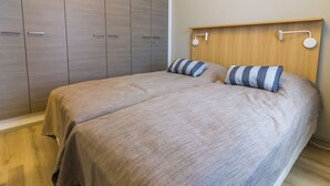 Un dormitorio con dos camas, un armario de madera y un cabecero con luces fijadas a la pared.