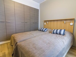 A bedroom with two beds, wooden wardrobe, and a headboard with wall-mounted lights. - Ylläs chalets 4203 by Interhome (Ylläsjärvi)