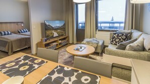 Una habitación de hotel moderna con sofá, una mesa de comedor, televisión y un ventanal con vista a un puente.