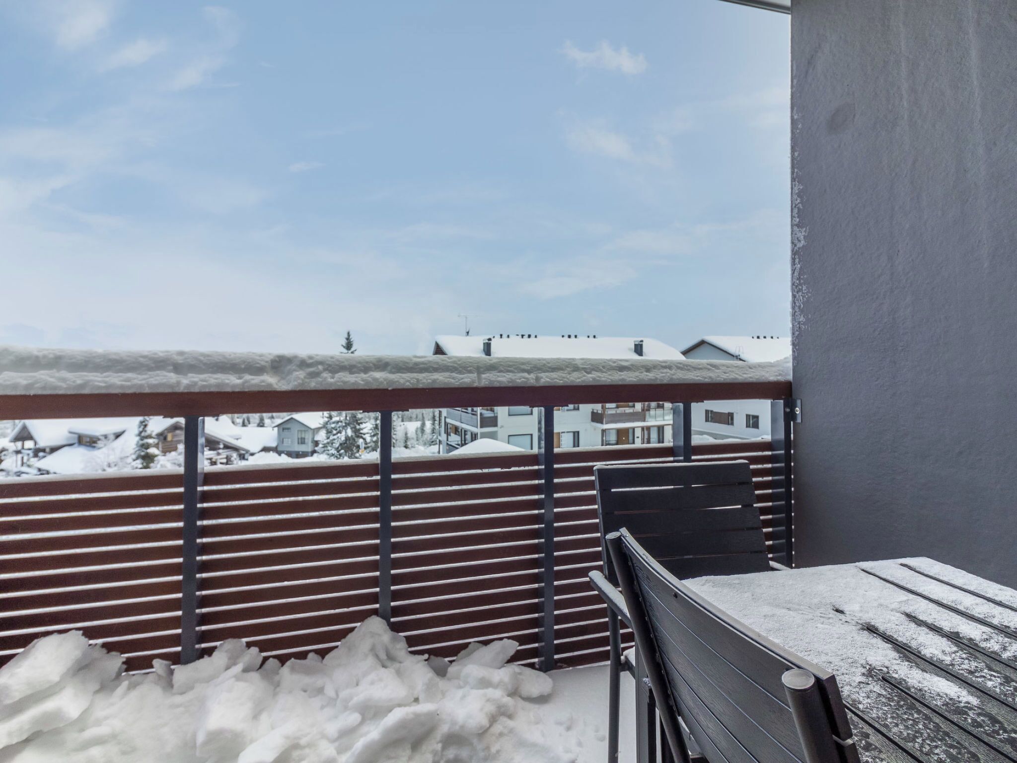 En balkon med gelænder af træ og en bænk, dækket af sne.