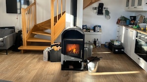 Een moderne woonkamer met een houten trap, een open haard, een keuken met witte kasten en een flatscreen televisie aan de muur.