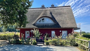 Een rood huis met rieten dak, houten omheining en een grindpad.
