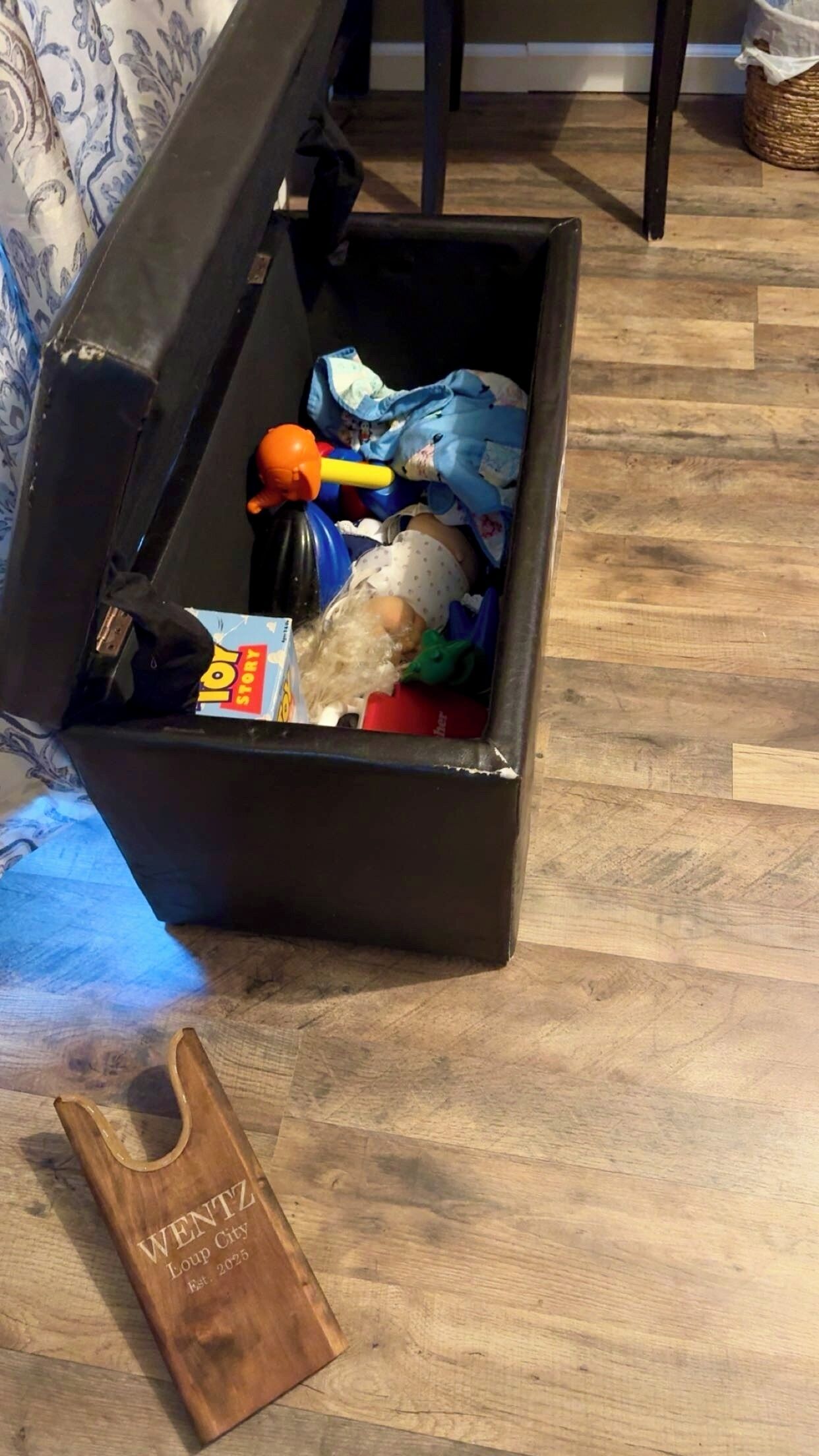 Eine schwarze Aufbewahrungsbox auf einem Holzboden, neben ihr eine braune Tasche mit dem Aufdruck 'WENTZ Loup City'.