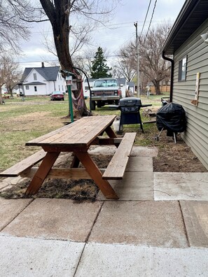 Una mesa de picnic con una parrilla y un árbol al fondo.