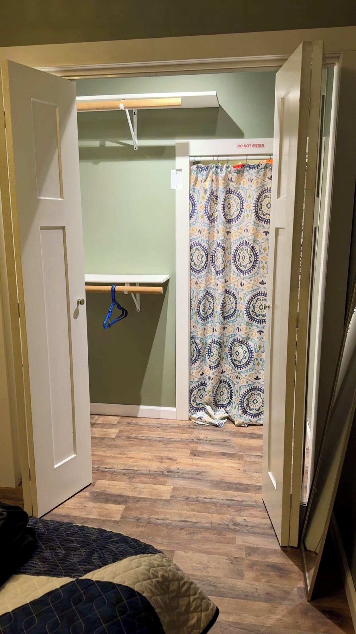 A room with a bed, a door, a curtain, and a hanging rack.