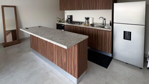 A modern kitchen with a central island, wooden cabinets, a built-in stove, and a stainless steel refrigerator. - Modern 2BR Retreat | Pool, Wi-Fi, AC & Prime Location, 10 Min from Everything (Puerto Vallarta)