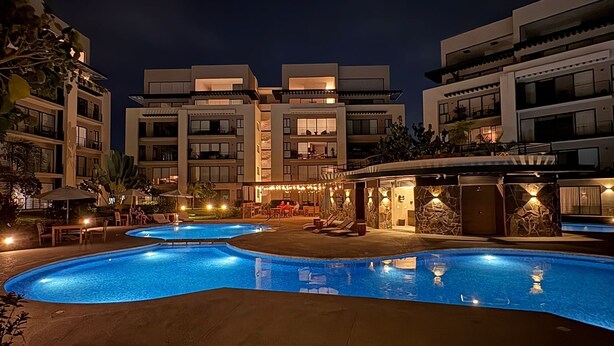 A nighttime view of a hotel with a swimming pool, outdoor seating, and modern architecture. - Modern 2BR Retreat | Pool, Wi-Fi, AC & Prime Location, 10 Min from Everything (Puerto Vallarta)