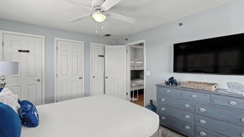 Une chambre à coucher avec un lit, une commode, un ventilateur de plafond et un téléviseur.
