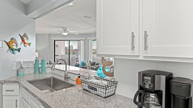 Eine moderne Küche mit Granit Arbeitsplatten, einer Edelstahl-Spüle, einer Kaffeemaschine und Fisch-Wandbildern.