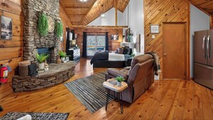A cozy cabin interior with a stone fireplace, wooden walls, a living area with a sofa and coffee table, and a kitchen with a refrigerator. - Hot Tub! Location! Cozy Studio Log Cabin,Fireplace (Gatlinburg)