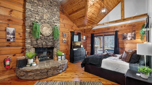 A cozy cabin interior with a stone fireplace, wooden walls, a bed, and a television. - Hot Tub! Location! Cozy Studio Log Cabin,Fireplace (Gatlinburg)