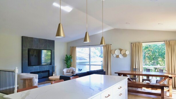 Una cocina moderna con una isla grande, luces colgantes, un televisor de pantalla plana y un comedor con mesa y sillas de madera.
