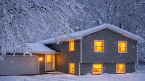 Una casa de dos pisos con garaje, rodeada de árboles cubiertos de nieve.