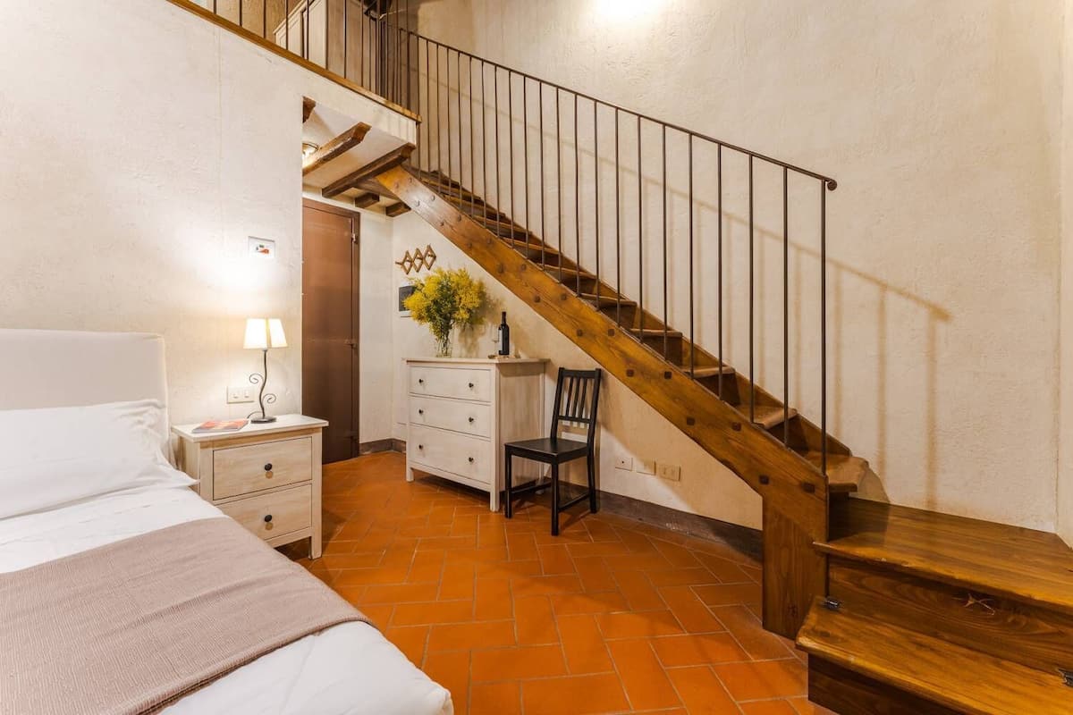 A bedroom with a wooden staircase, a bed, a nightstand, a dresser, and a chair.