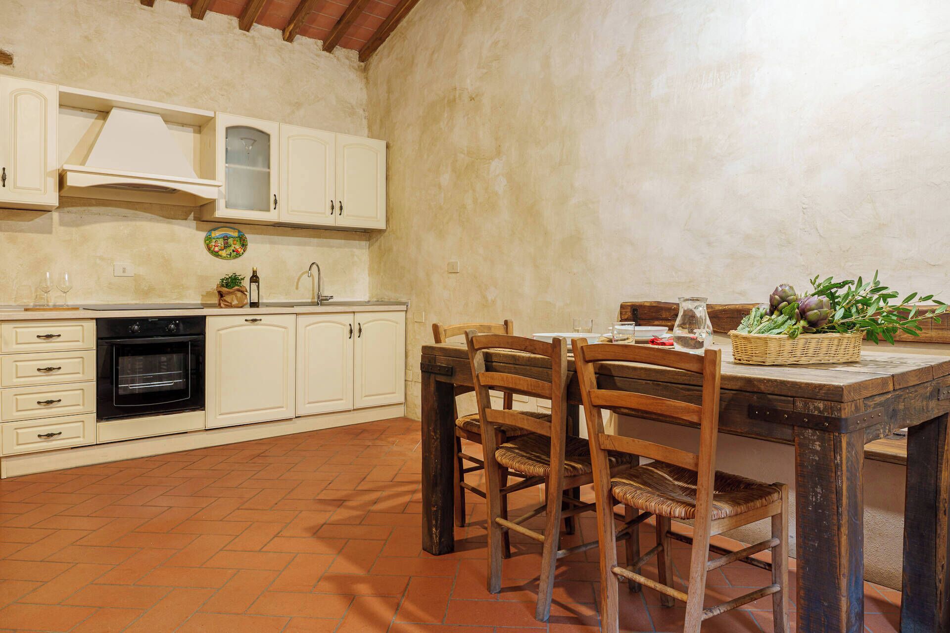 A rustic kitchen with white cabinets, a black oven, and a wooden dining table with chairs.