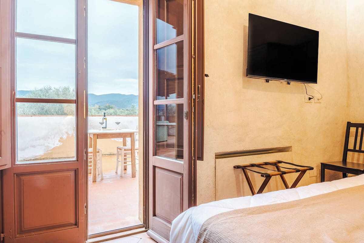 A bedroom with a bed, a TV mounted on the wall, and a balcony with a table and chairs.
